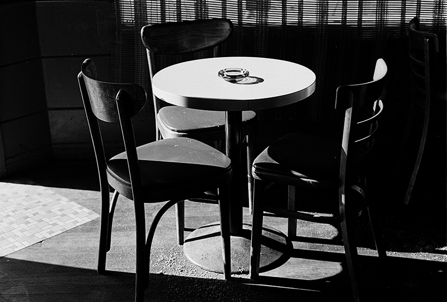 Black and White Photo of Table in Bar in Strong Diagonal Light.